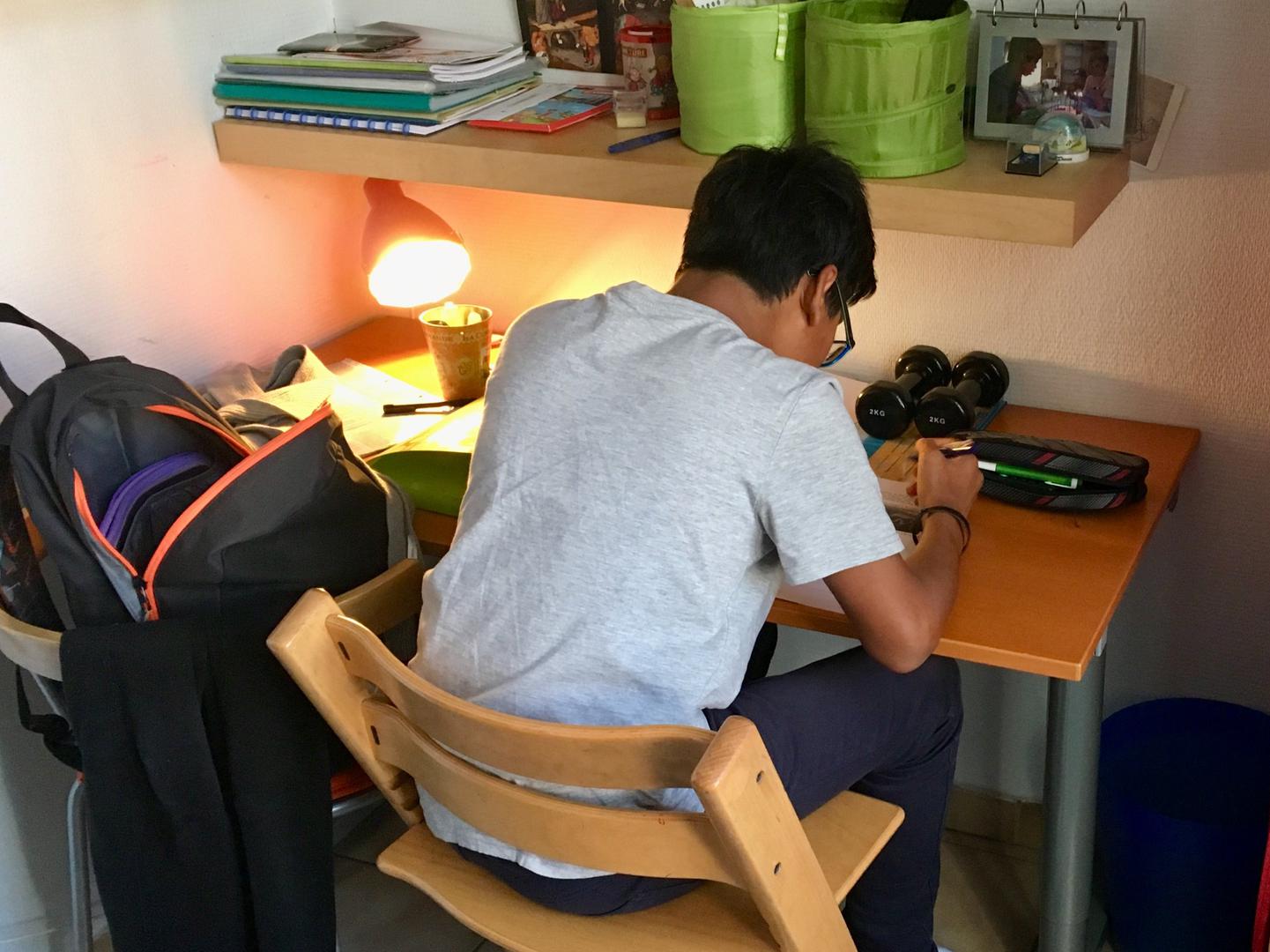 A boy sitting at his desk in his room doing homework