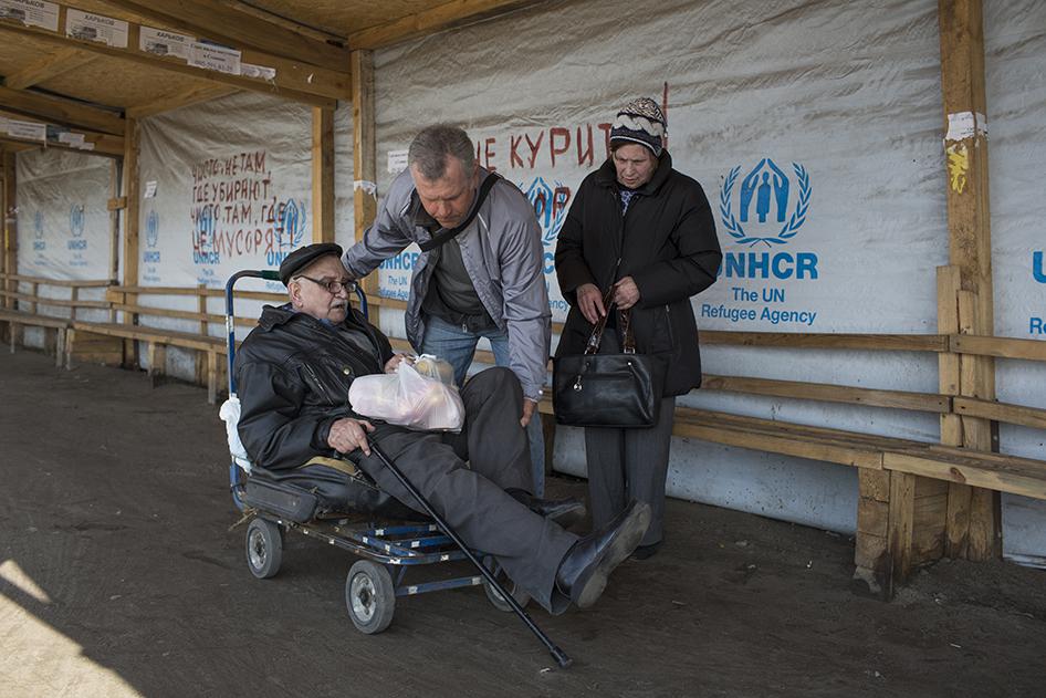 An older man with a disability sits on an old luggage cart preparing to cross the Stanitsa Luhanska border point in Eastern Ukraine.