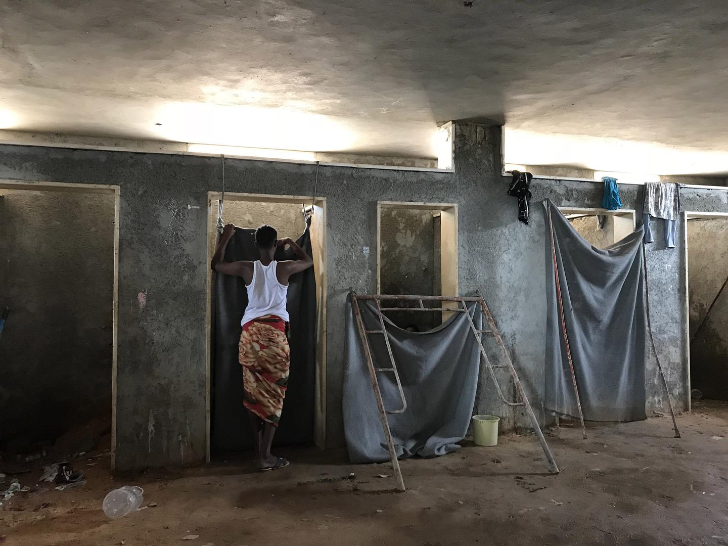 A detainee stands outside a toilet stall in the Ain Zara detention center, Tripoli, July 5, 2018. 