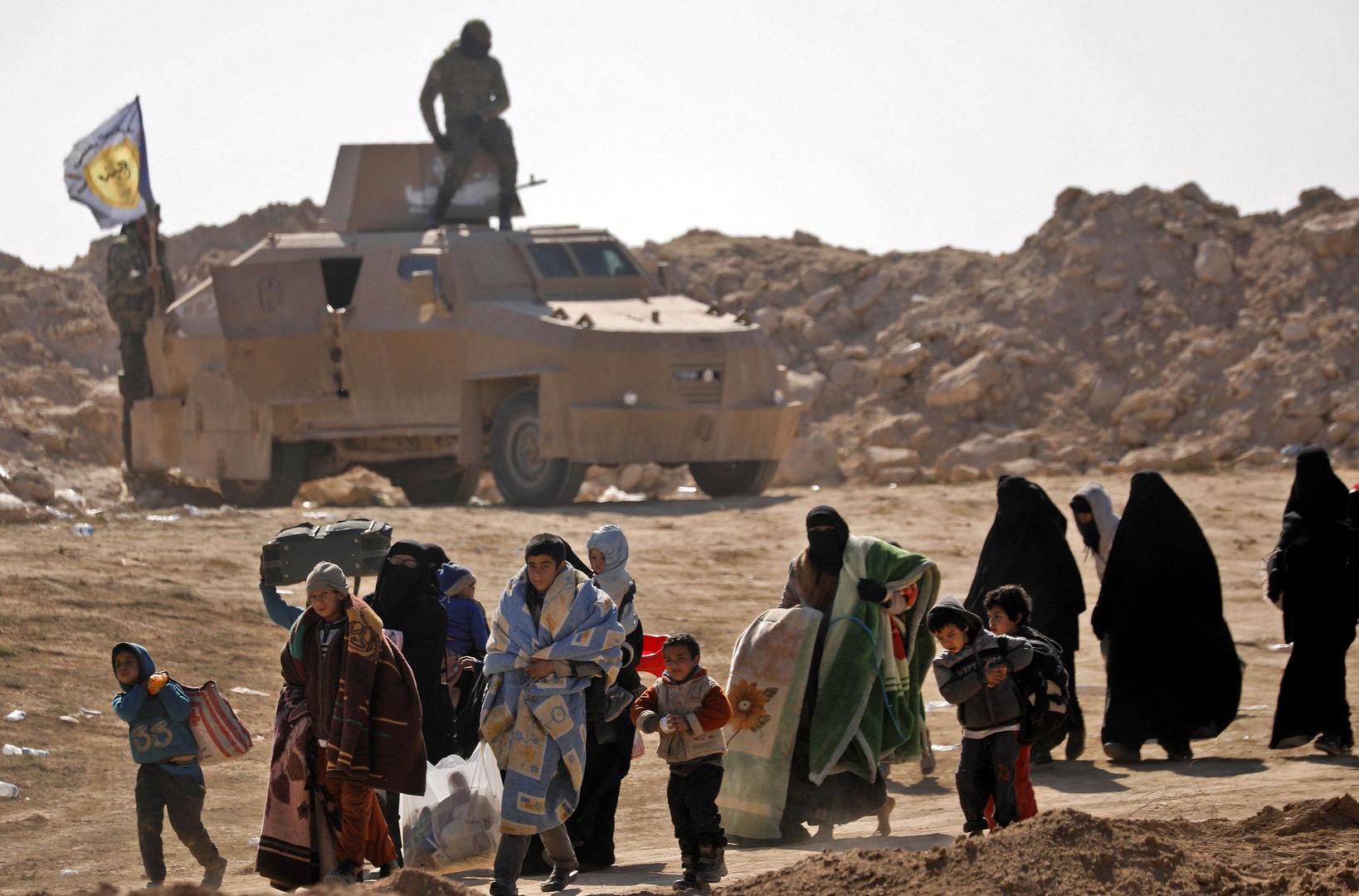 Civilians fleeing the battered ISIS-held holdout of Baghouz in the eastern Syrian province of Deir Ezzor walk past an armored vehicle belonging to the Manbij military council into a nearby area held by the Syrian Democratic Forces (SDF) on February 12, 20