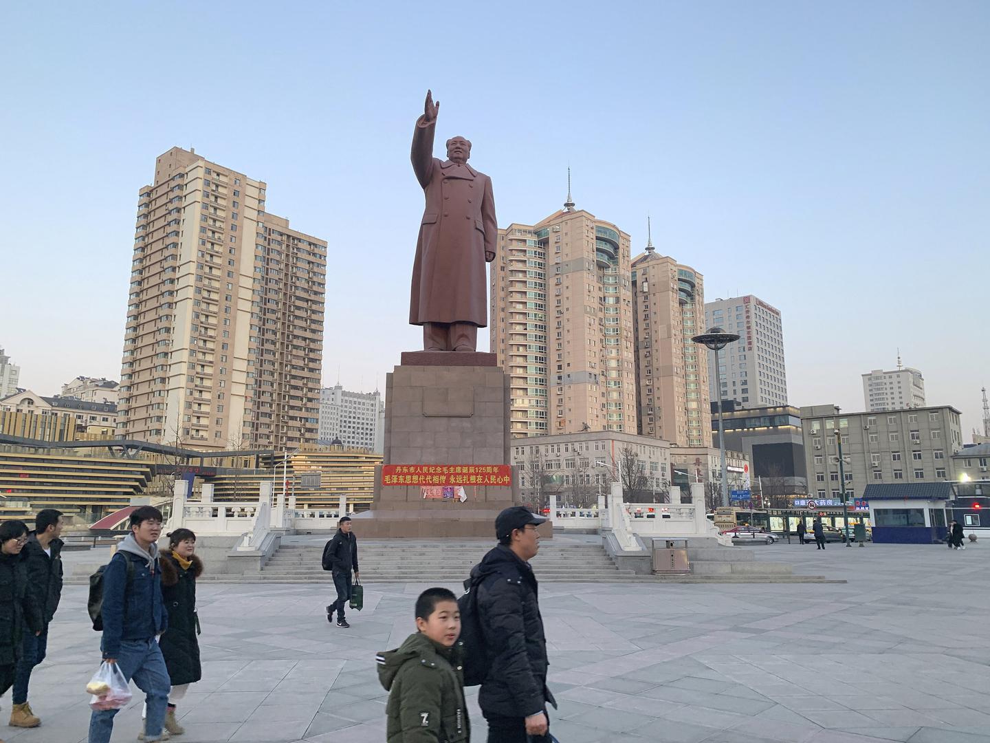 中国东北辽宁省靠近朝鲜边境的丹东市，行人走过火车站前的毛泽东铜像，摄于2019年2月23日星期六。