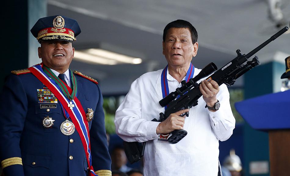 Le président des Philippines Rodrigo Duterte, à droite, tenant un fusil offert par Ronald "Bato" Dela Rosa, à gauche, lors d’une cérémonie marquant la fin du mandat de Dela Rosa en tant que chef de la Police nationale, au Camp Crame à Quezon City au nord-