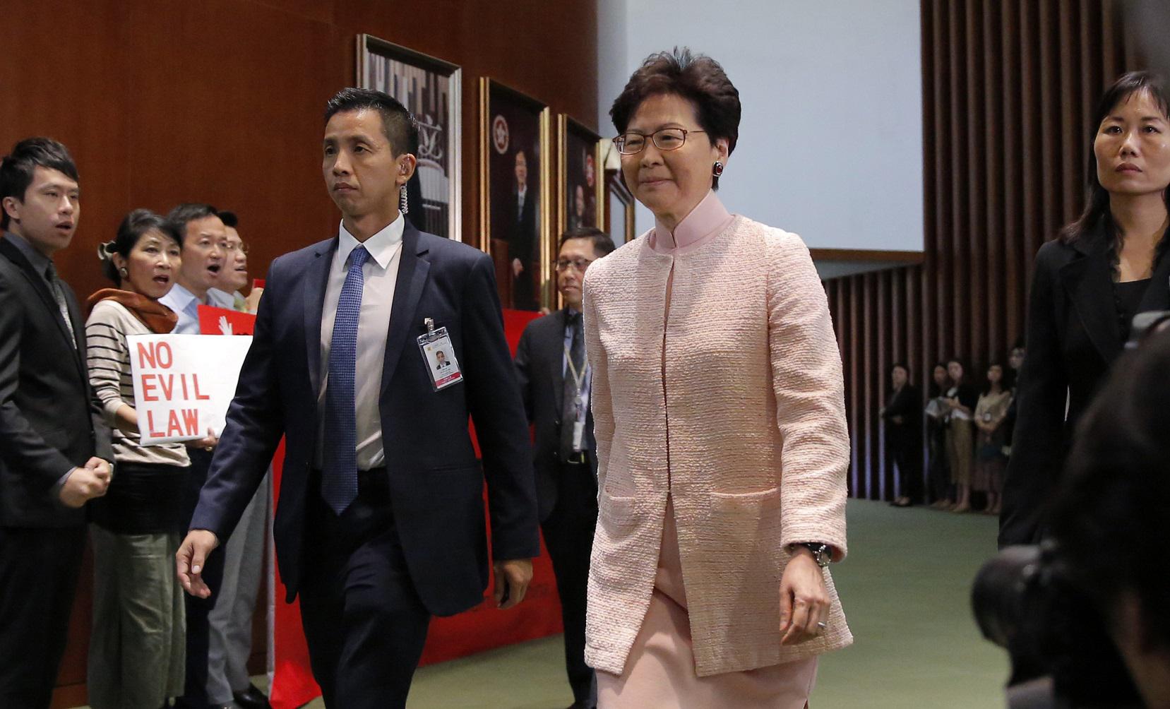 FILE - In this May 22, 2019, file photo, Hong Kong Chief Executive Carrie Lam, center, arrives for a meeting at the Legislative Council as the pro-democracy lawmakers chant placard and banner against the new extradition law in Hong Kong. Hong Kong's gover