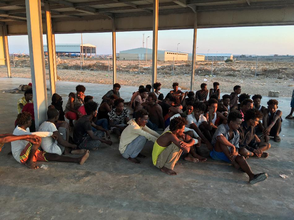 Rescued migrants sit on a coast some 100 kilometers (60 miles) east of Tripoli, Libya