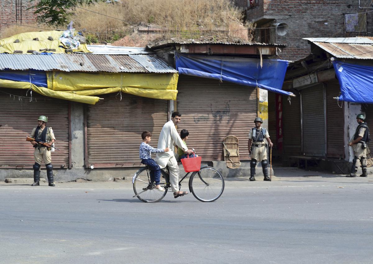 Un homme roule à bicyclette avec deux enfants devant des forces de sécurité indiennes lors de la période de couvre-feu à Srinagar, au Cachemire, le 17 août 2019.
