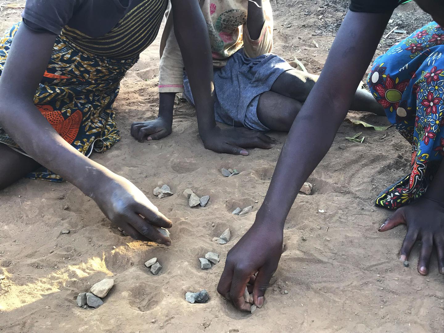 Trois jeunes filles jouent avec des cailloux en guise de pions (jeu « isolo ») sur un terrain sableux dans la commune de Waya à Kabwe, en Zambie. Or, elles s’exposent ainsi à des poussières de plomb toxique, dont les taux sont particulièrement élevés dans