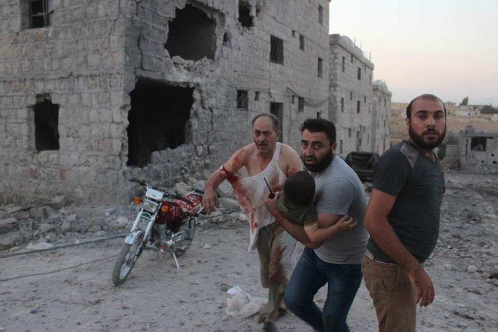 Residents rescue injured child after strike on the displacement center in Hass on August 16, 2019.