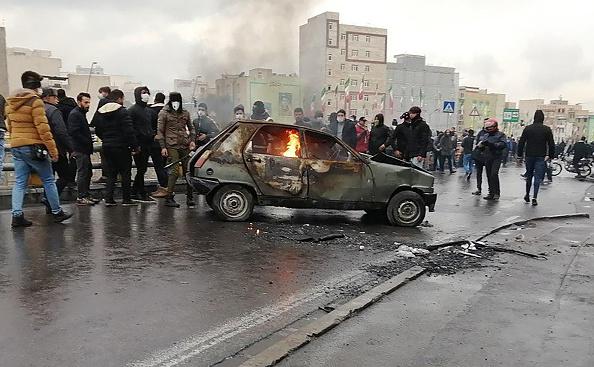 معترضان ایرانی در جریان تظاهرات علیه افزایش قیمت بنزین اطراف ماشینی در حال سوختن در پایتخت، تهران، در ۱۶ نوامبر ۲۰۱۹
