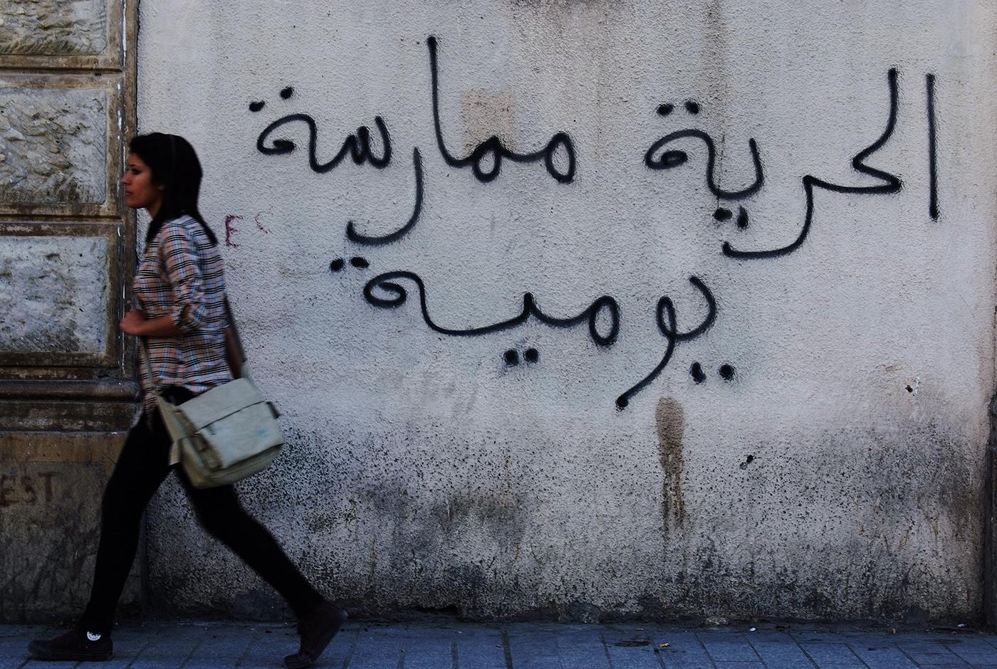 A Tunisian woman walks past a graffiti that reads "Freedom is a daily practice" in Tunis April 26, 2011.