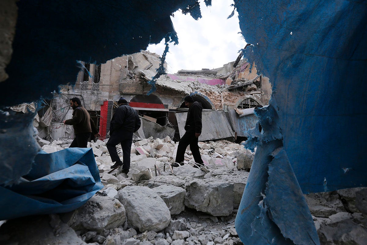 People walk past destruction from government airstrikes in the town of Ariha, in Idlib province, Syria, January 15, 2020.