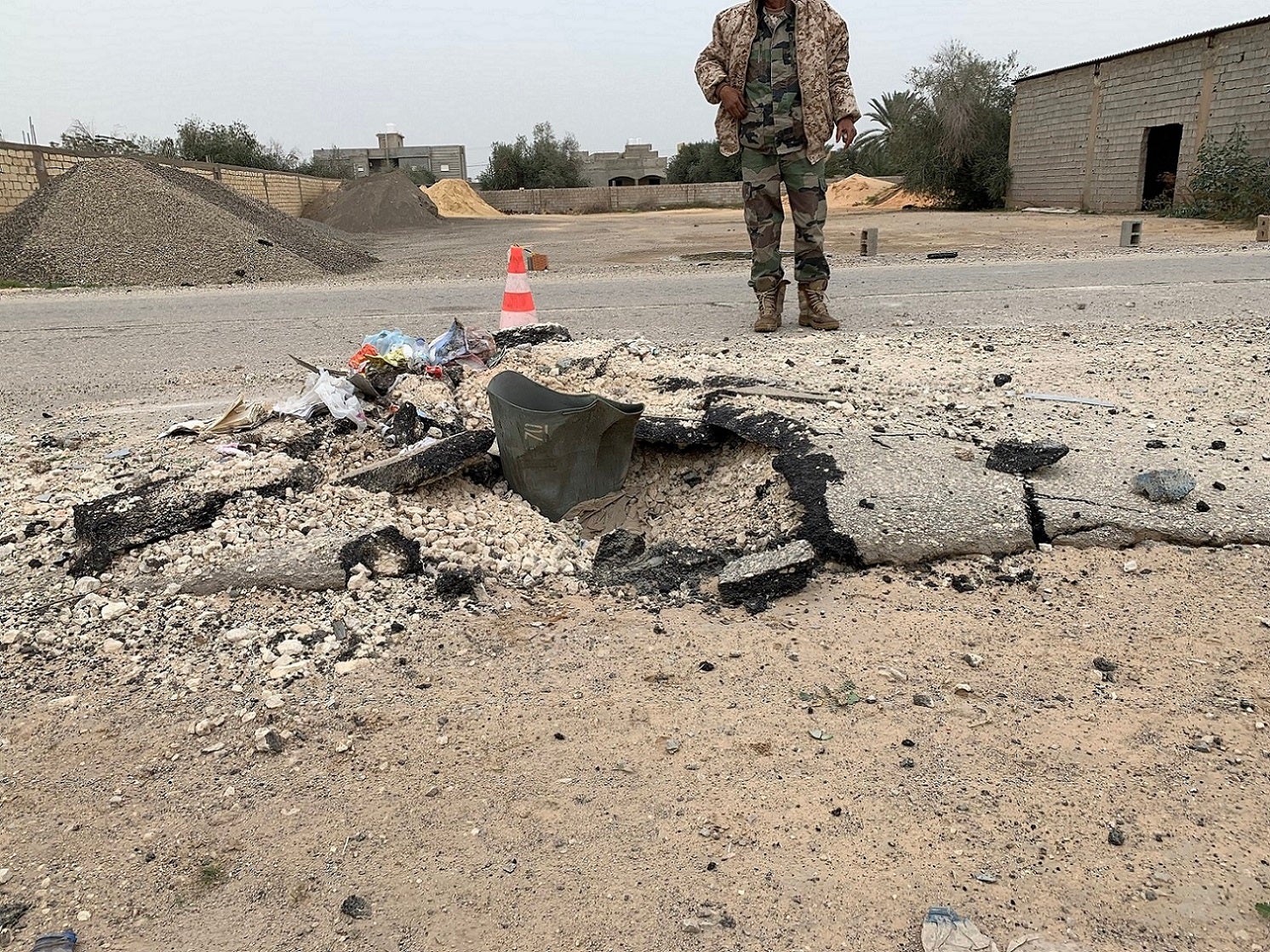 GNA checkpoint guard stands behind an expended cargo section of an RBK-250 PTAB-2.5M cluster bomb impacted into Alasfah Road near Tripoli International Airport following an attack on or around December 2, 2019, Tripoli outskirts, Libya, December 18, 2019.