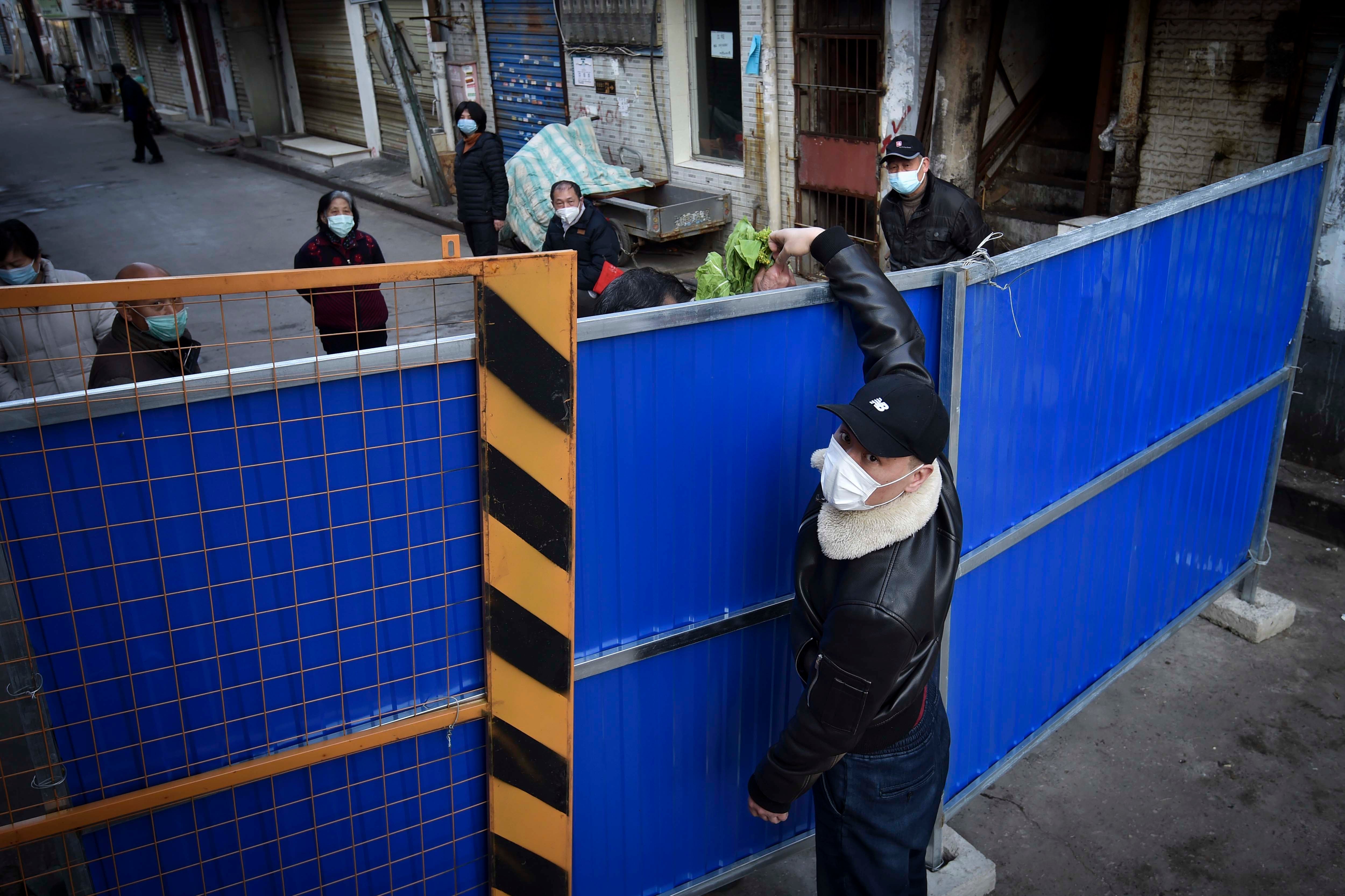 武汉一名戴口罩男子隔著围篱将食品送进被隔离社区，中国湖北，2020年2月23日。