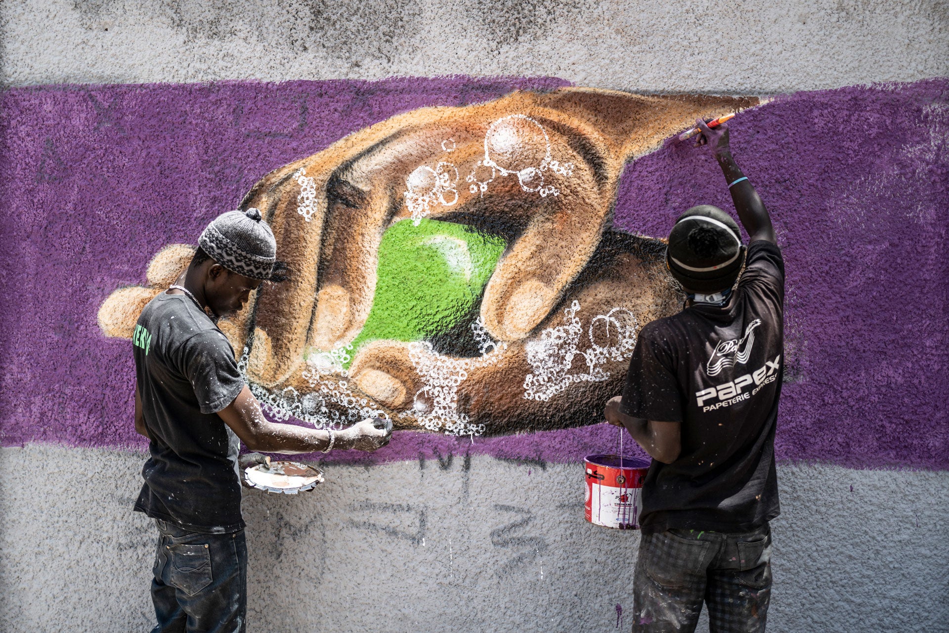 Deux membres du collectif sénégalais RBS CREW, spécialisé dans l’art du graffiti, travaillent sur une peinture murale illustrant le lavage de mains, préconisé pour se protéger contre le coronavirus. Cette photo a été prise devant le mur d'un lycée du quar