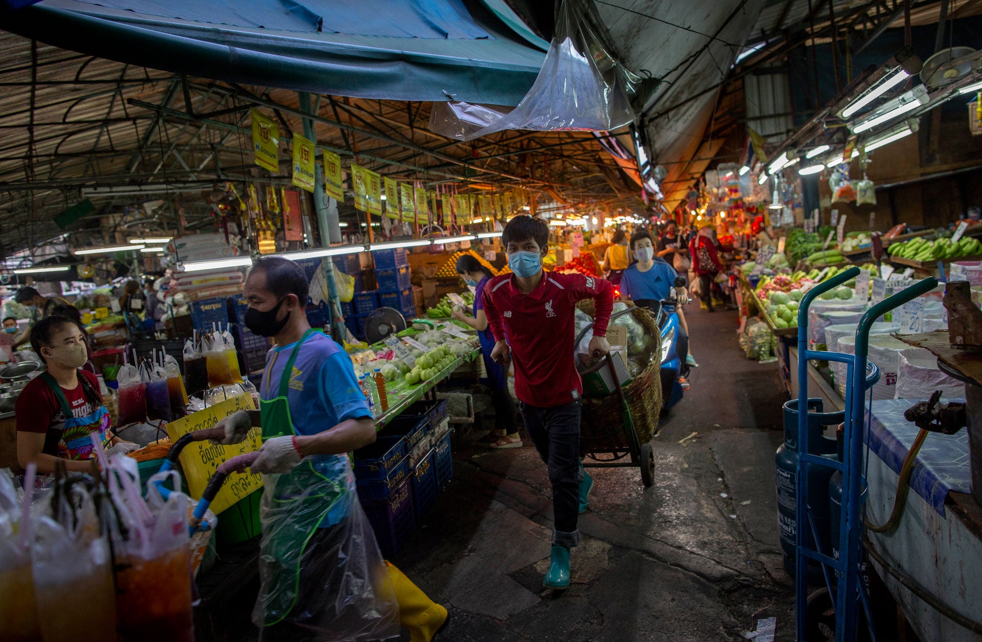 2020년 4월 9일, 태국 방콕의 청과물 시장에서 마스크를 착용한 사람들이 좁은 통로를 따라 수레를 끌고 있다.