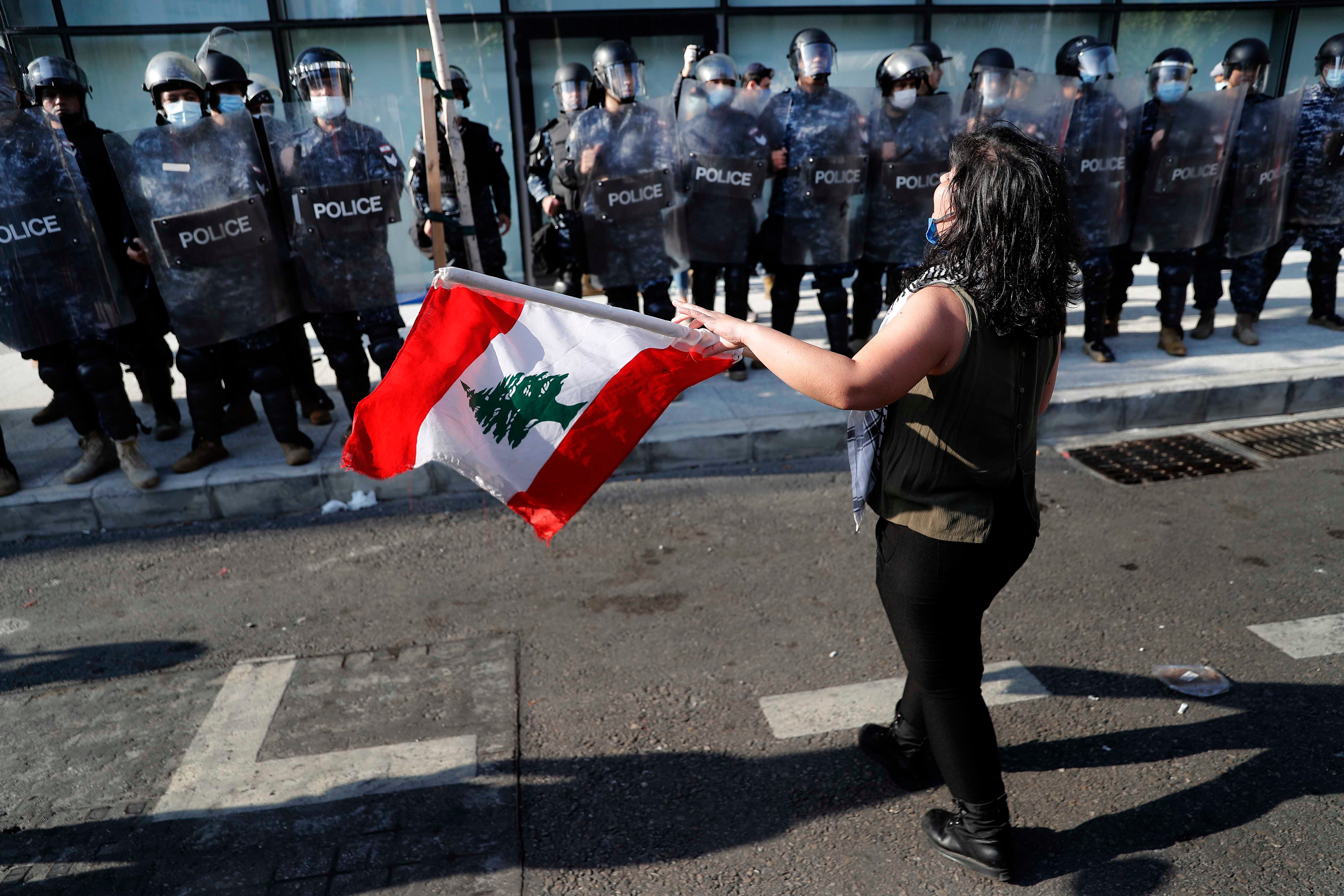 An anti-government protester holds a Lebanese flag in front the riot police during a protest against the deepening financial crisis, in Beirut, Lebanon, Tuesday, April 28, 2020.