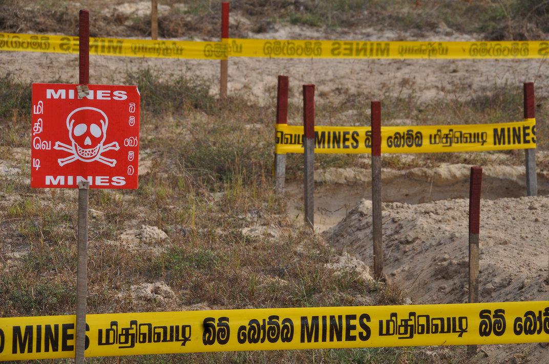 A mine field in Sri Lanka is marked with Danger! Mines! signs and caution tape.