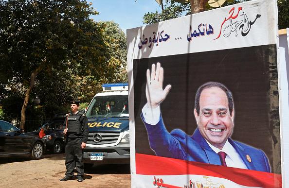 Egyptian policemen standing guard outside a polling station with an electoral banner depicting incumbent President Abdel Fattah al-Sisi seen with a caption reading in Arabic 'for the sake of Egypt we will continue the story of a nation', in the capital Ca