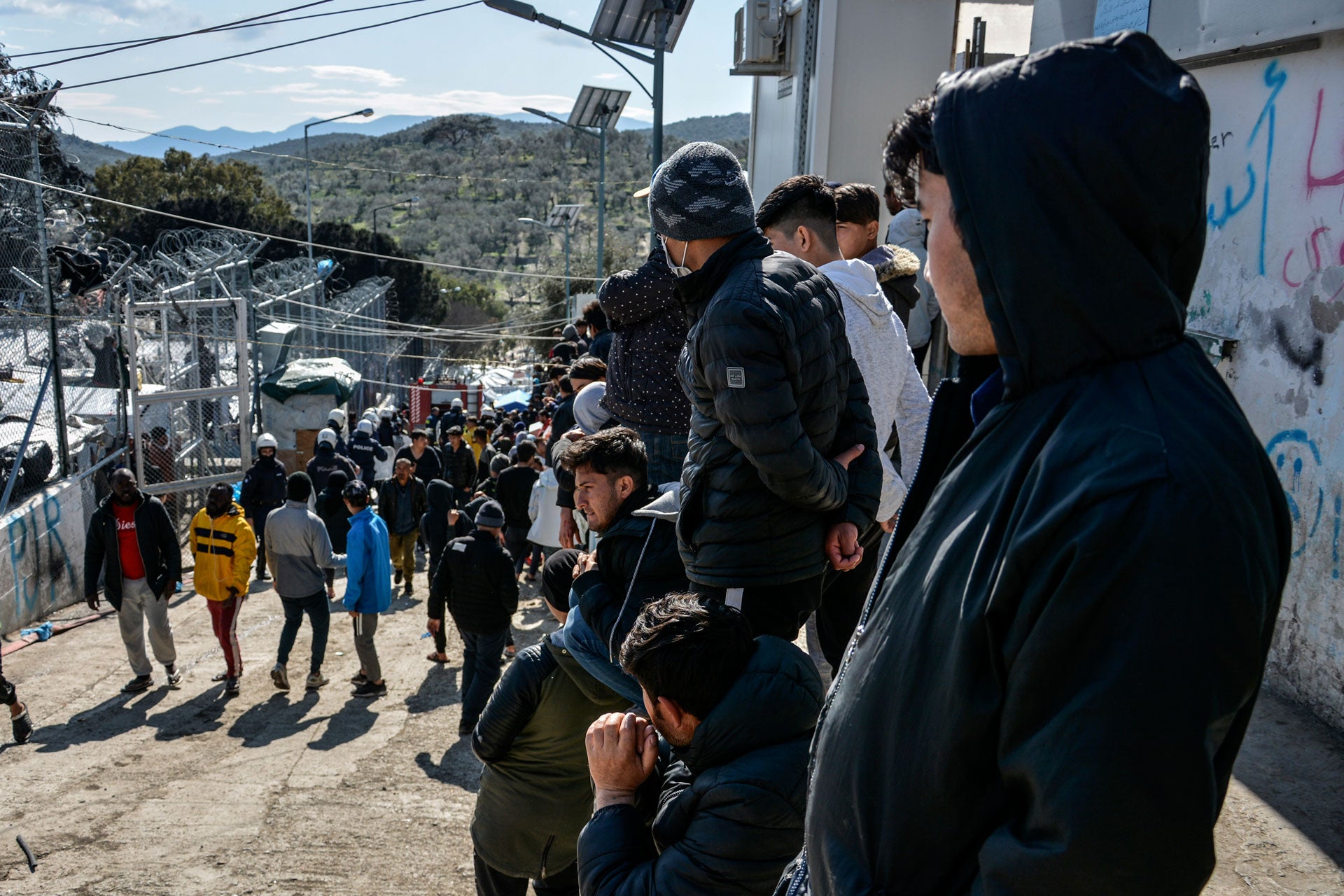 Migrants gather as riot police guard a gate in Moria refugee camp on the northeastern Aegean island of Lesbos, Greece, March 16, 2020. 