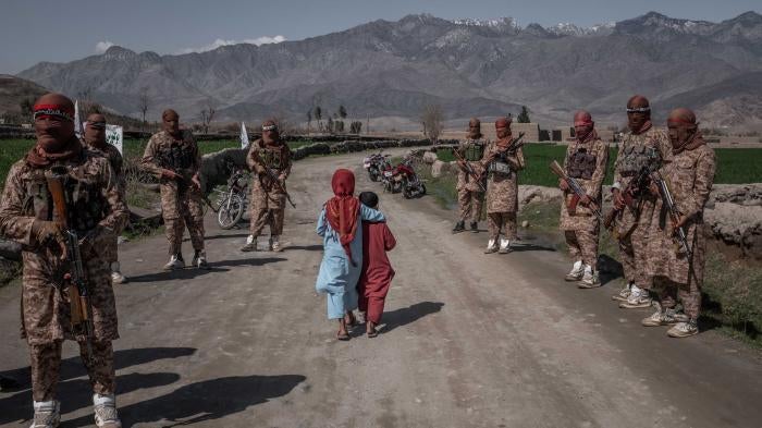 Two children walk by armed soldiers in the countryside