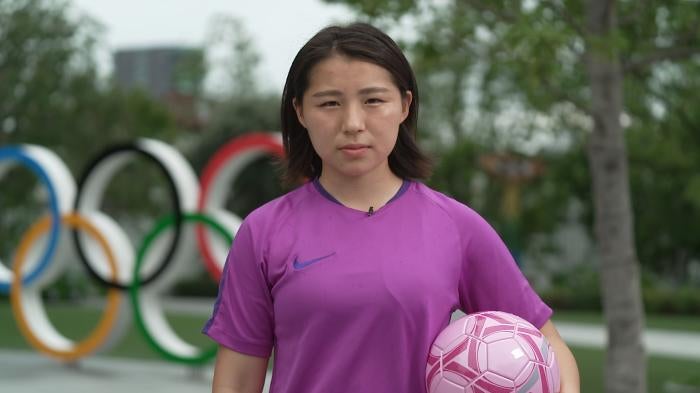 Soccer player holding ball in front of Olympic rings