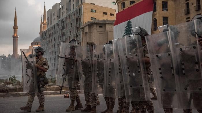 Riot police with shields in front of Lebanese flag