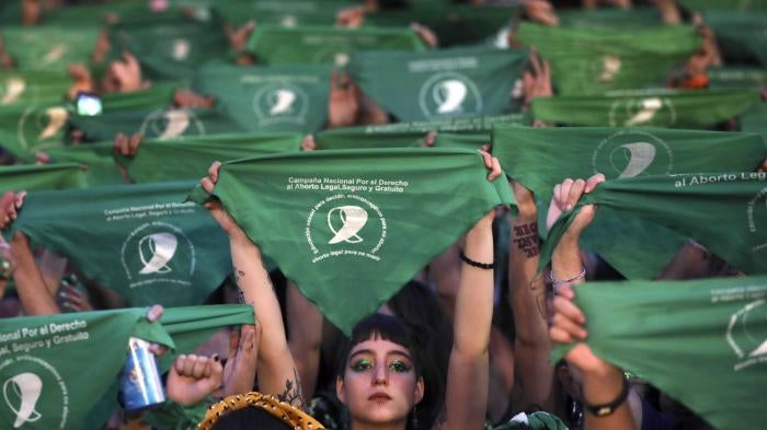 A crowd of women hold up green protest signs