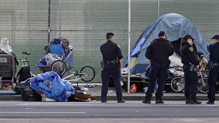 Police officers wait while people experiencing homelessness collect their belongings during a sweep of their encampment under a San Francisco, California freeway, March 1, 2016. 