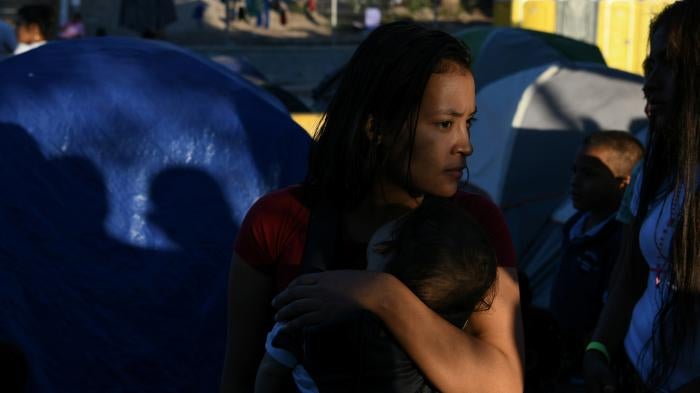 A woman holds a child in front of a group of tents