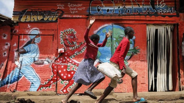 Children run past a mural that warns people about the dangers of the new coronavirus, in the Kibera informal settlement of Nairobi, Kenya.