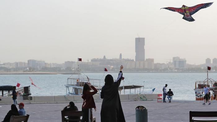 Women fly a kite in a park next to a body of water