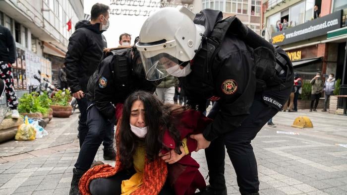 Police forcefully detain a protester  who is crying on the ground while the police stand over her at a demonstration. 