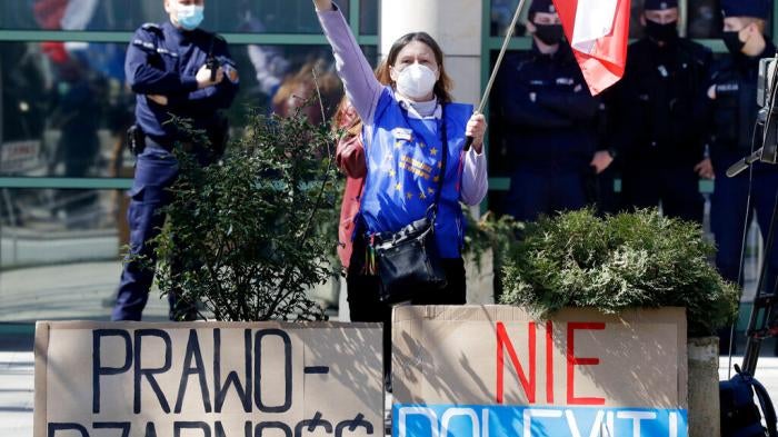 A pro-EU protestor stands outside the Constitutional Tribunal in Warsaw, Poland, on April 28, 2021 with posters that say Rule of Law and No Polexit! 