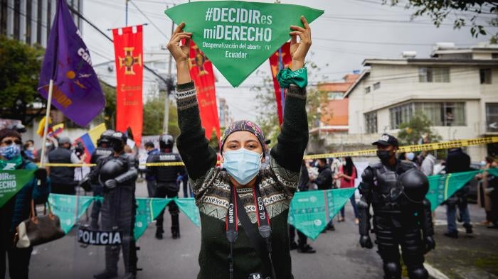 A masked woman in a protest on the street holding up a green flag