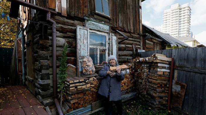 A pensioner carries logs in the courtyard of her wooden house where she opened a private museum of the old quarter.