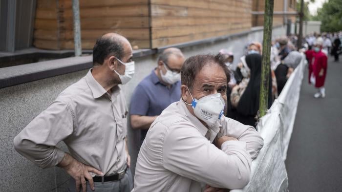 An Iranian man wearing a protective face mask looks on as people line-up to receive China's Sinopharm vaccine in central Tehran on July 19, 2021. 