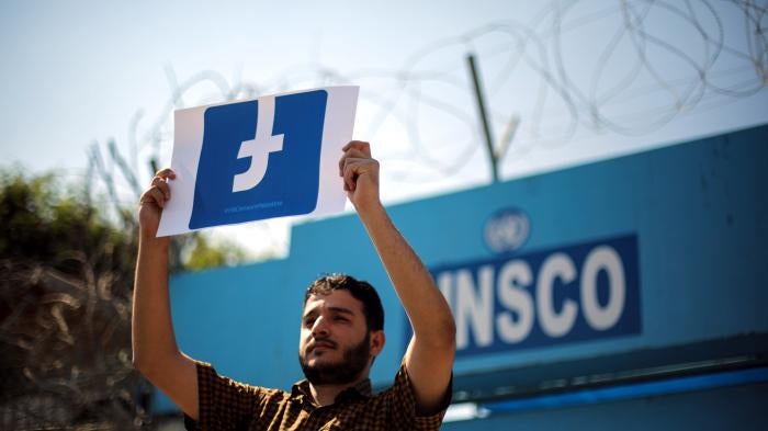 A Palestinian demonstrator holds a banner of the Facebook logo.