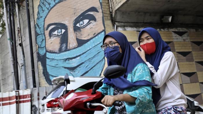 Women ride a motorbike past a large Covid-19-themed mural in Jakarta, Indonesia, October 2, 2020.