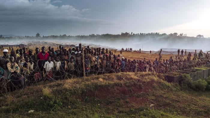 Dozens of people gather along the fence of the Rhoo displaced persons camp in Ituri in northeastern Democratic Republic of Congo, December 21, 2021
