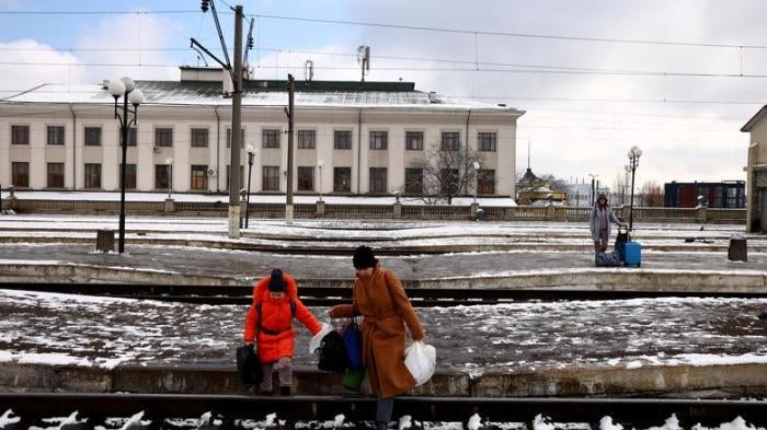 People fleeing Russia's invasion of Ukraine, cross train tracks to get to a train leaving for Poland, at the train station in Lviv
