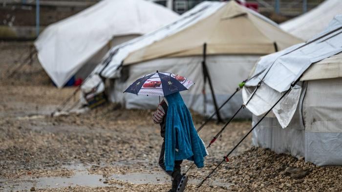 A young person holds an umbrella as he walks in the rain at Camp Roj, where relatives of people suspected of belonging to the Islamic State (IS) group are held, in Syria's northeastern Hasakah province, on March 4, 2021. 