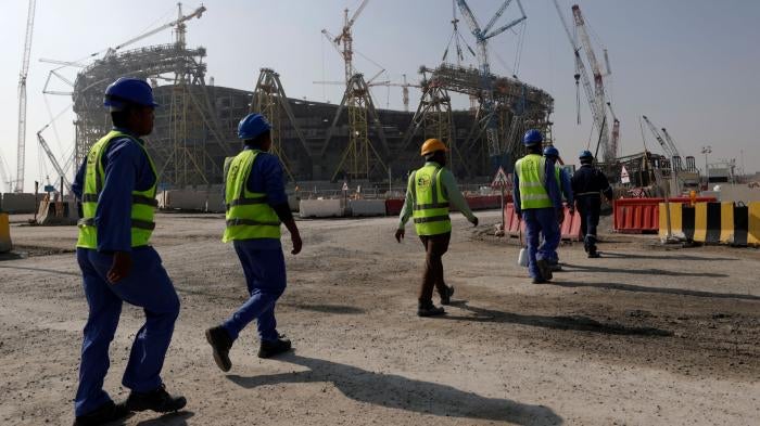 Workers walk toward a sports stadium under construction