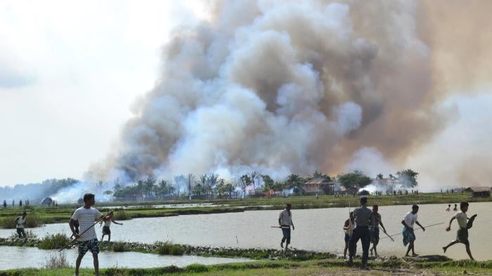 Ethnic Rakhine with weapons walk away from a village in flames while a soldier stands by, June 2012.