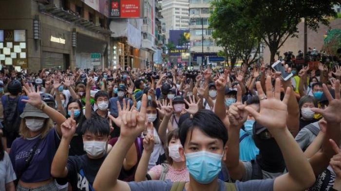A crowd of protesters holding up five fingers on one hand, and one finger on the other hand.