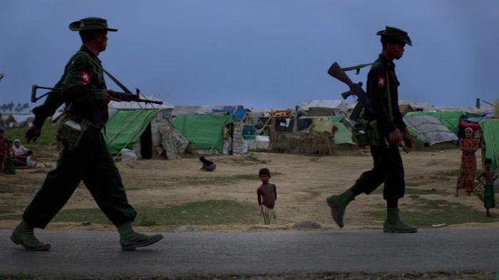 A Rohingya boy watches soldiers patrol his camp