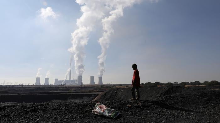 A child collects coal in front of a coal-fired power plant