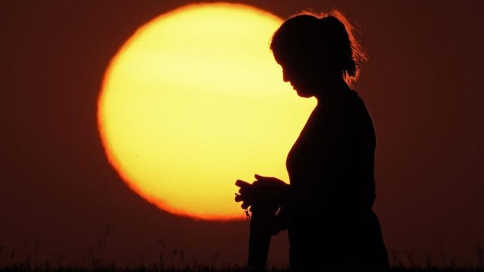 A woman stands in front of a setting sun