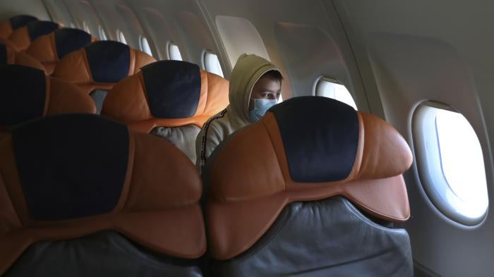 A boy in a face mask sits alone on an airplane