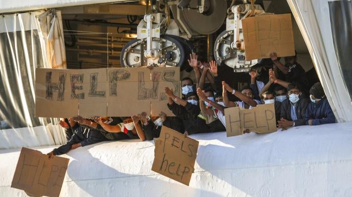 Migrants hold banners asking for help from a deck of the Geo Barents rescue ship operated by Doctors Without Borders, in Catania's port, Sicily, southern Italy, November 7, 2022