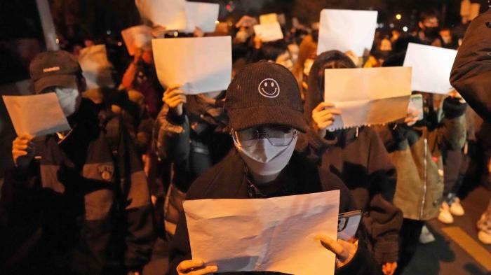 Protesters hold up blank papers and chant slogans as they march in protest in Beijing