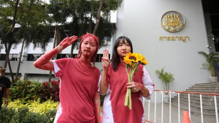 Orawan Phuphong and Tantawan Tuatulanon protest in front of the Bangkok Criminal Court by pouring red paint on themselves.